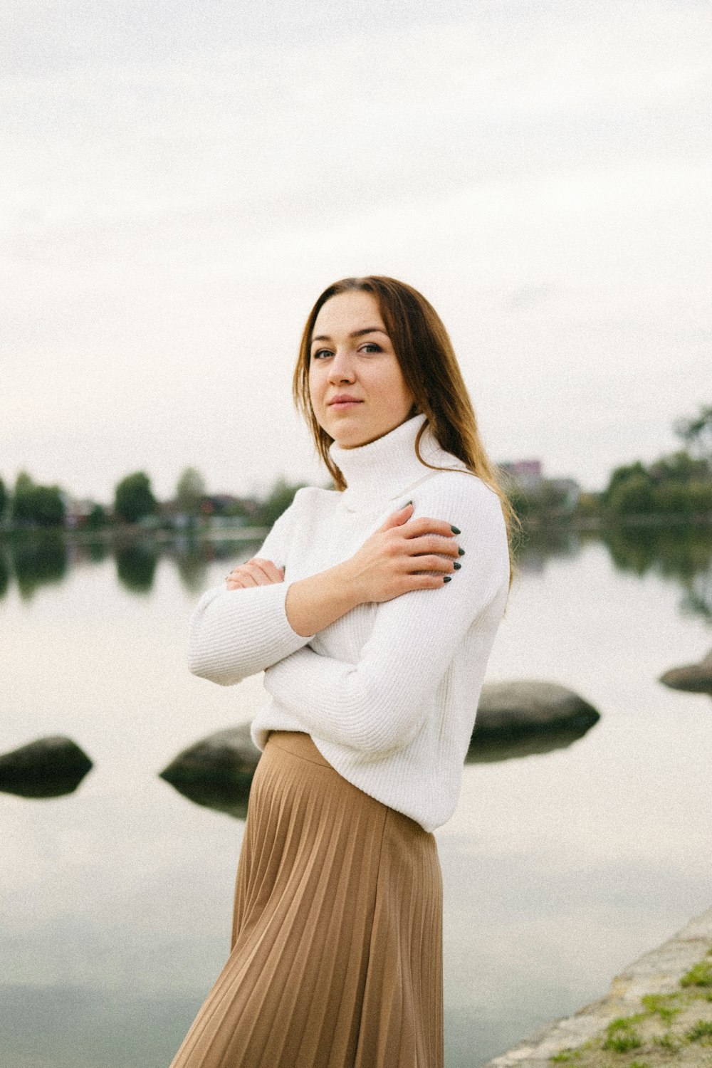 donna in camicia bianca a maniche lunghe e gonna marrone in piedi vicino al lago durante il giorno