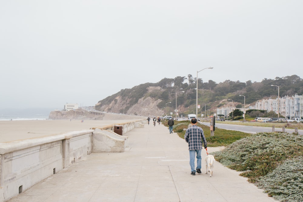 man in blue and white plaid dress shirt and blue denim jeans walking on gray concrete