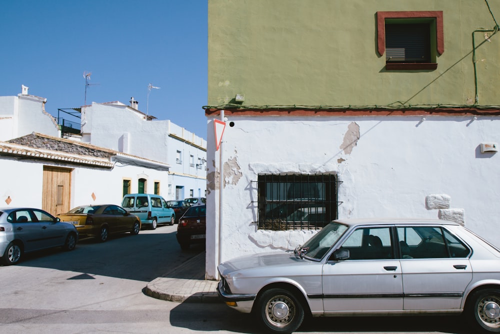 white sedan parked beside white concrete building during daytime