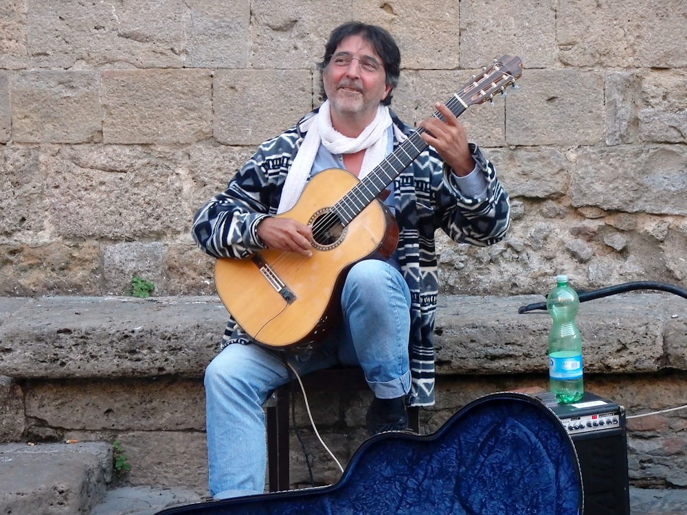 man in black and white jacket holding brown acoustic guitar