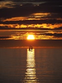 A panoramic view of the sailboat cutting through the water with fiery sunset clouds overhead.