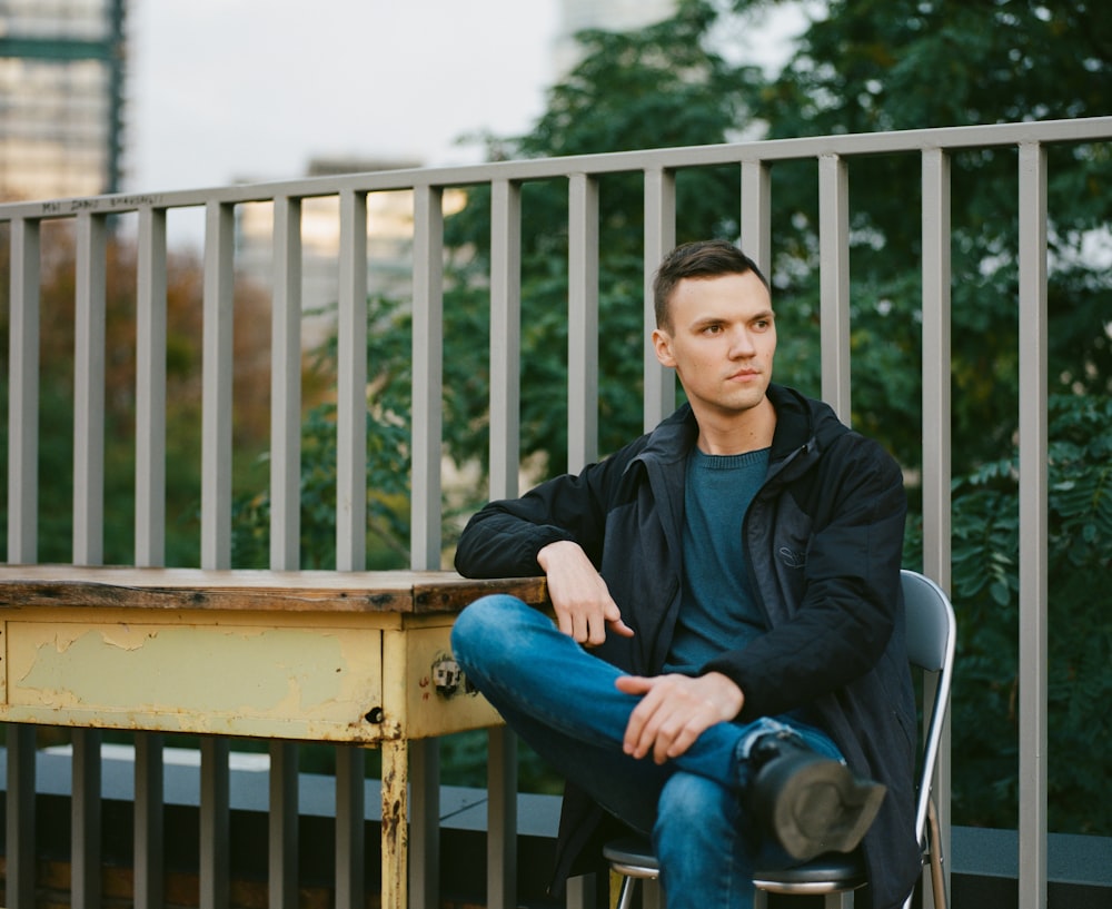 man in black jacket sitting on brown wooden bench