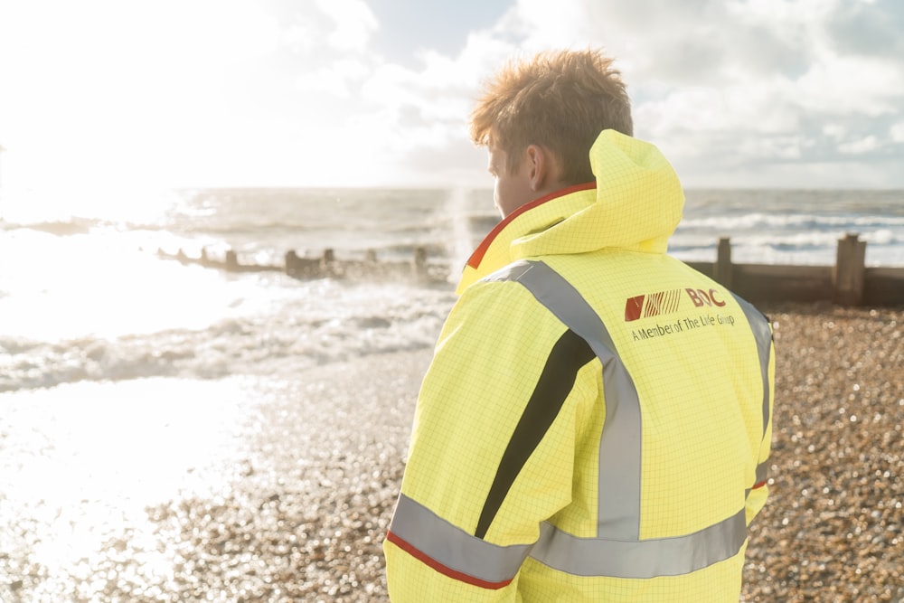 homme en veste jaune et blanche debout sur la plage pendant la journée