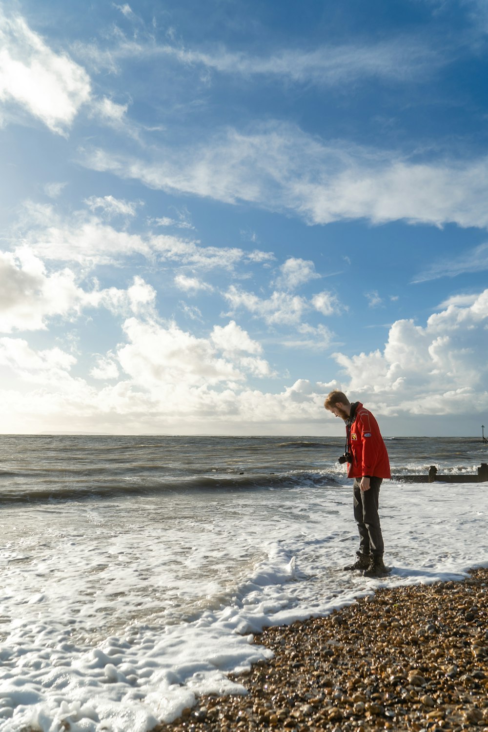 woman in red jacket standing on beach during daytime