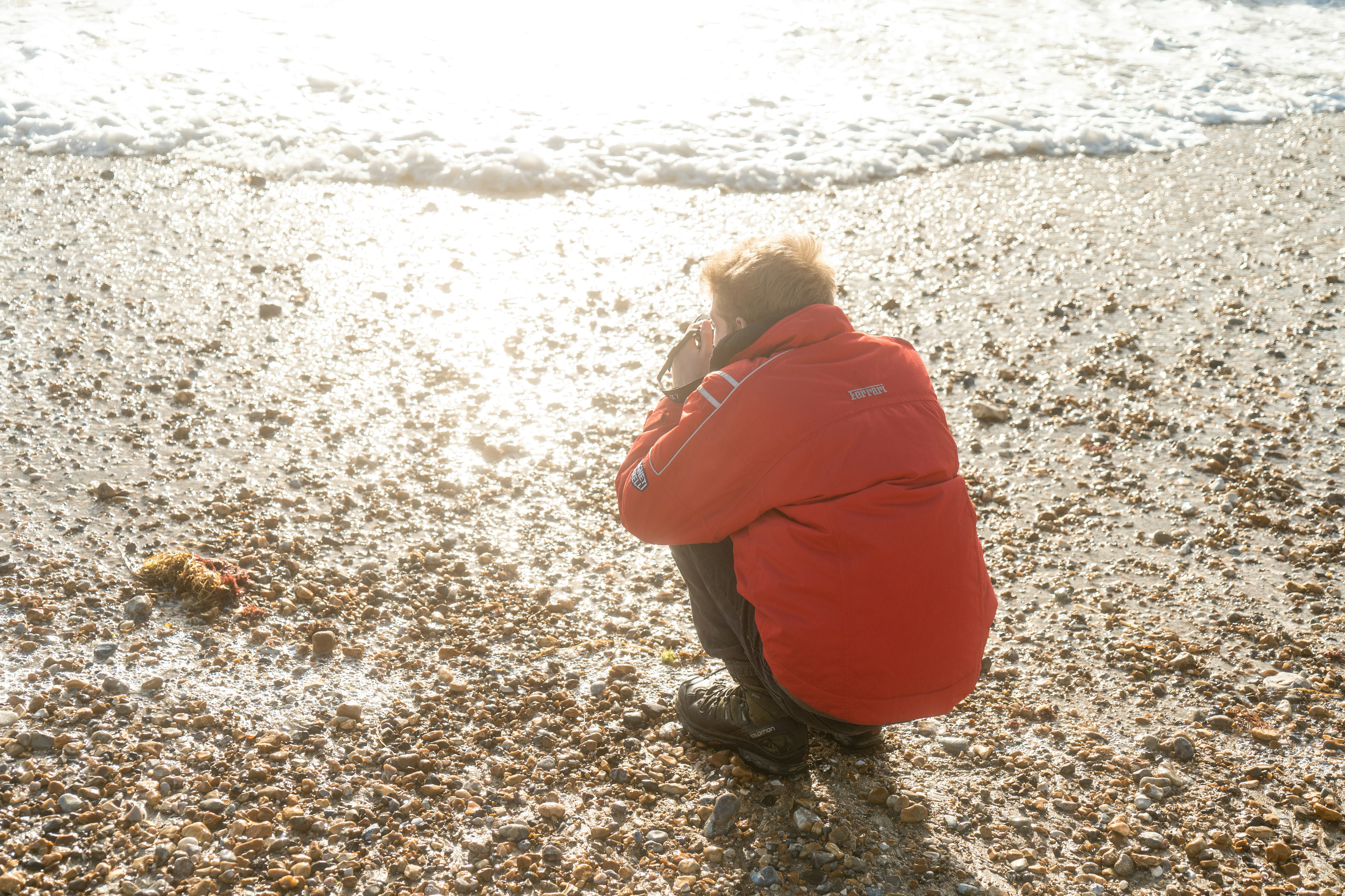 woman in red hoodie sitting on beach during daytime