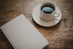 Close-up of a steaming cup of coffee beside an open book on a wooden table