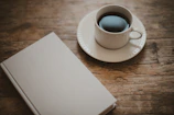 A rustic wooden table with a cup of coffee and a novel beside it.