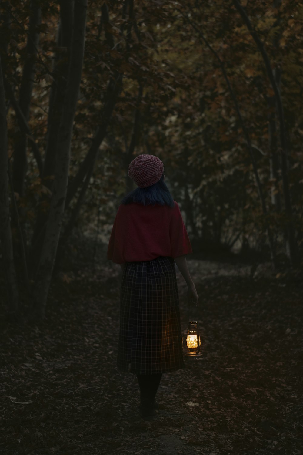 Frau mit lila Strickmütze und schwarzem Kleid im Wald stehend