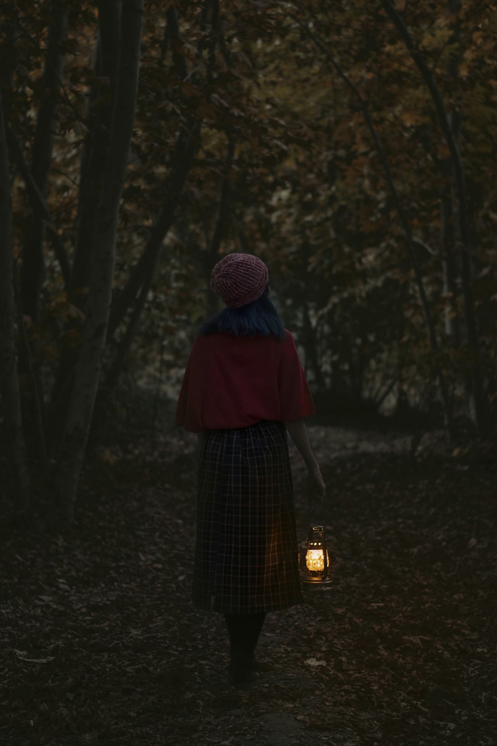 Mujer con gorro de punto púrpura y vestido negro de pie en el bosque