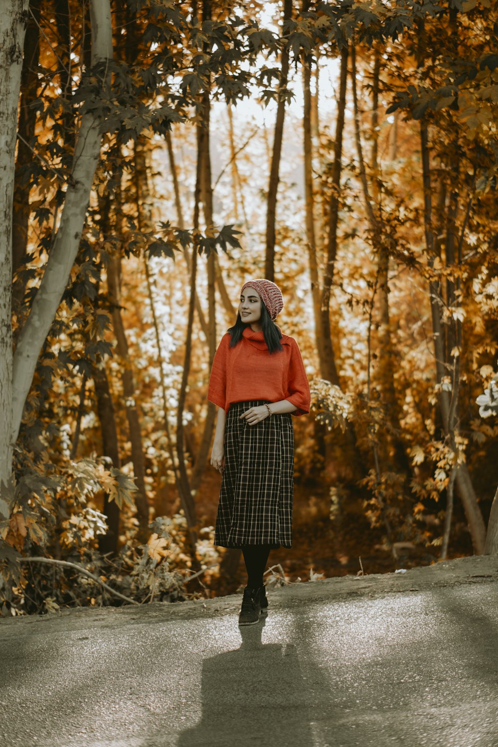 woman in black and white plaid coat standing on pathway surrounded by trees during daytime