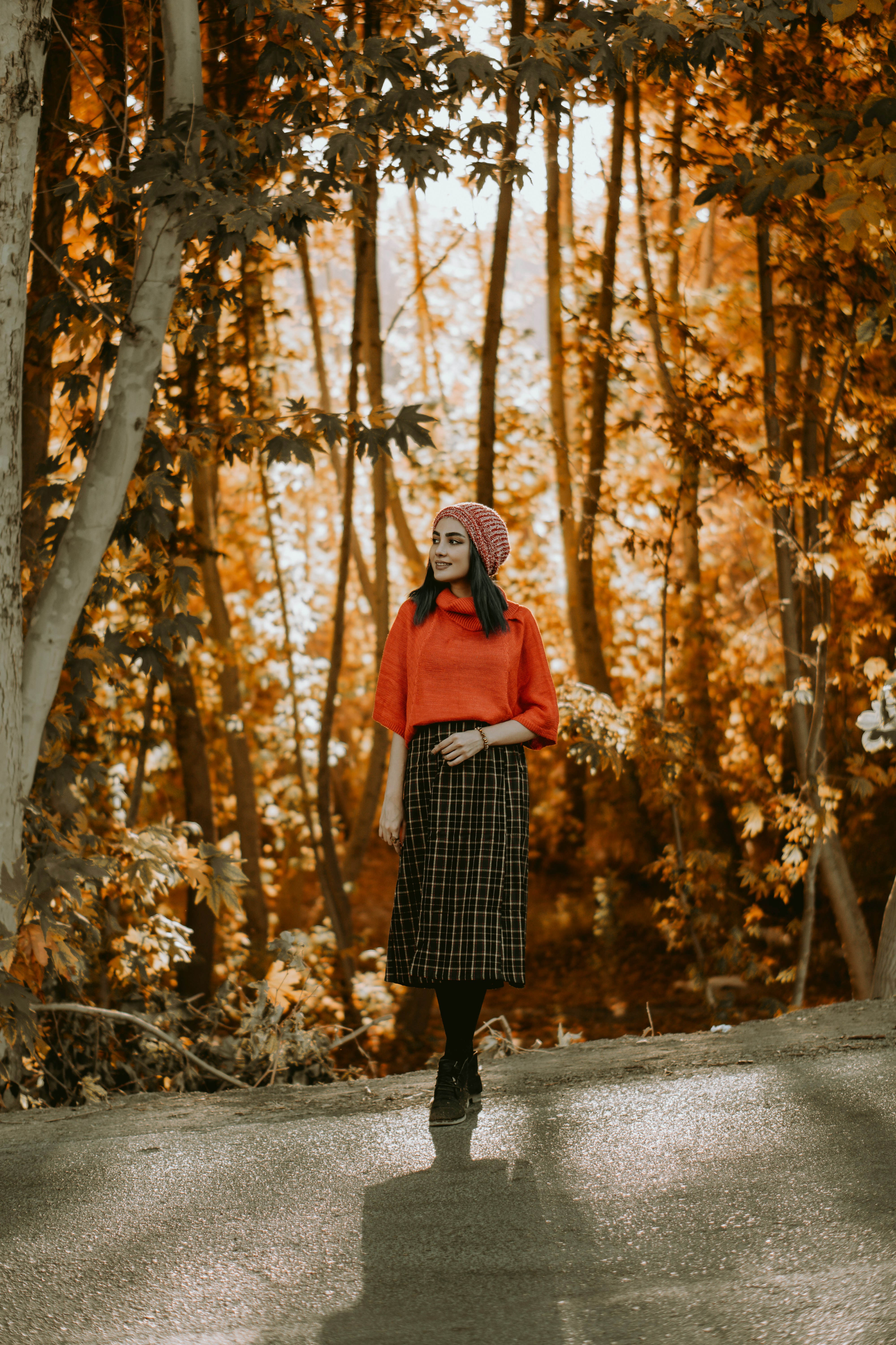 woman in black and white plaid coat standing on pathway surrounded by trees during daytime