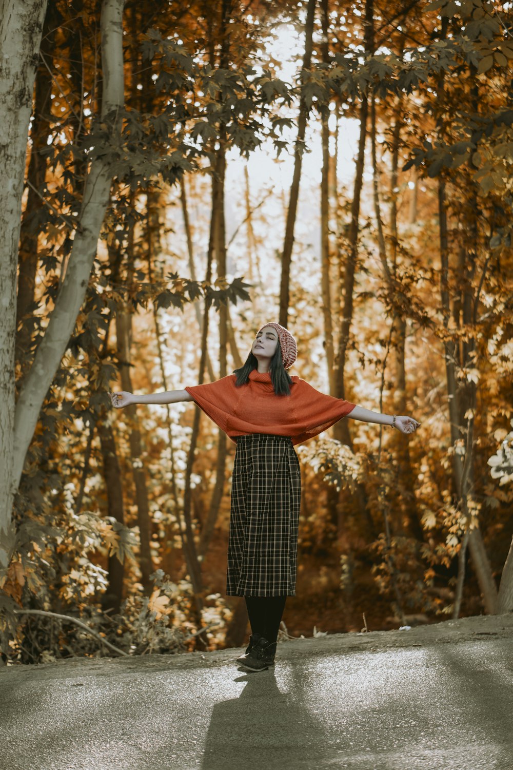 woman in red hoodie and black and white plaid skirt standing on forest during daytime