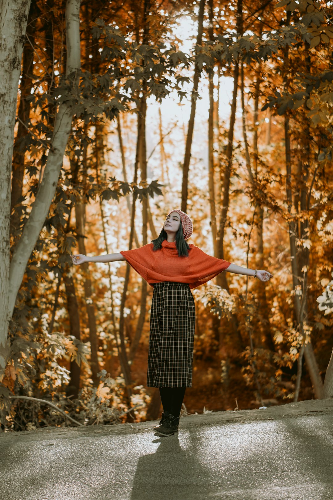 woman in red hoodie and black and white plaid skirt standing on forest during daytime