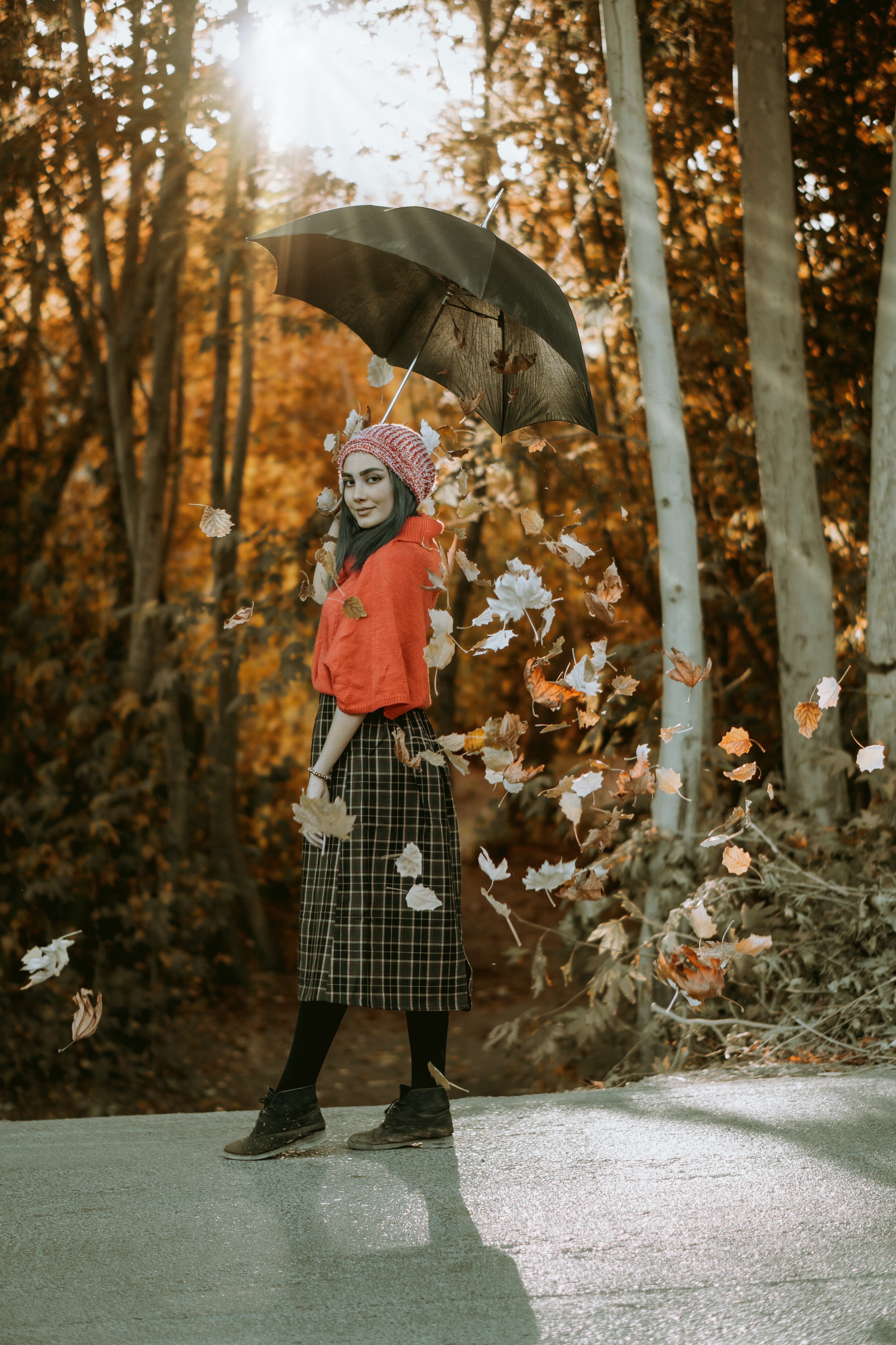 woman in red jacket and blue and white plaid skirt holding umbrella standing on forest during