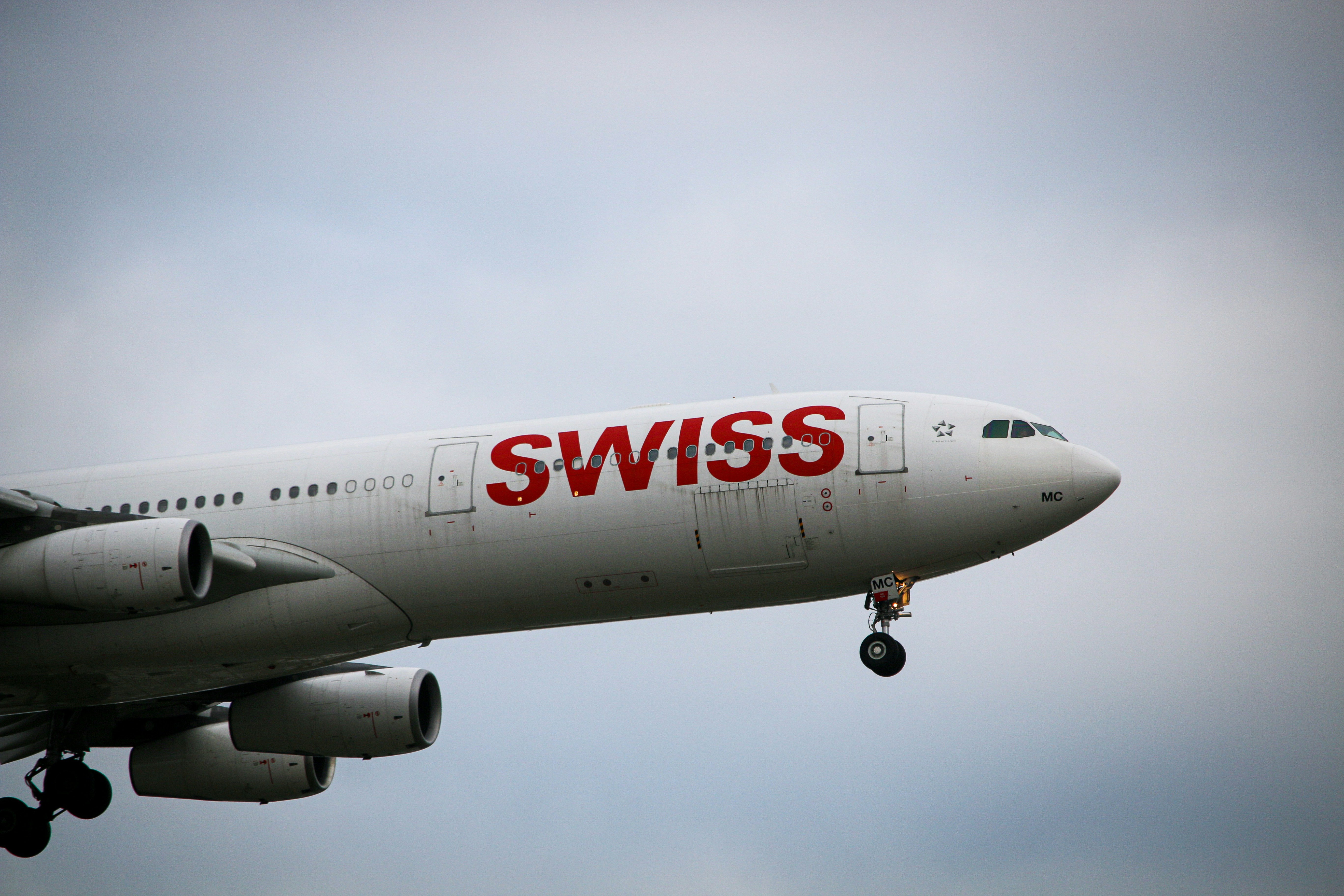 white and red air plane under white clouds during daytime, Swiss Airlines A340 on final for runway 22L after their new resumed route from Zurich.