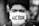 A close-up black and white photograph of a person wearing a white face mask with the word 'HÉROE' written on it. The background is blurred, highlighting the subject's face prominently.