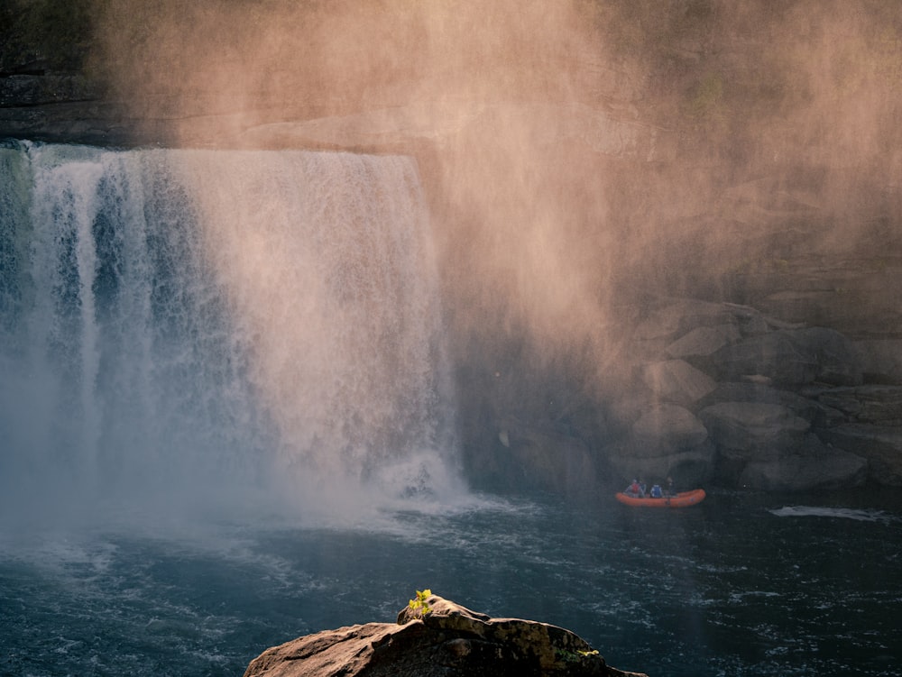 man in red jacket sitting on rock near water falls during daytime