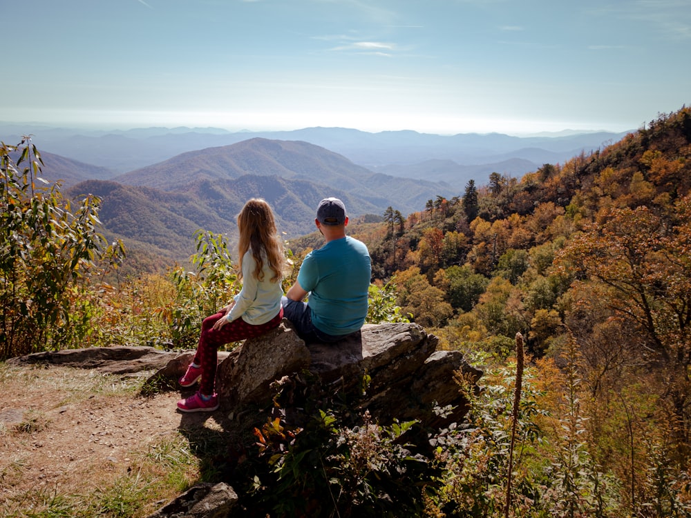 woman in blue long sleeve shirt sitting on rock during daytime