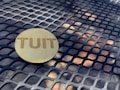 A wooden circular token with the word 'TUIT' engraved on it lies on a metal grid table with a geometric pattern.