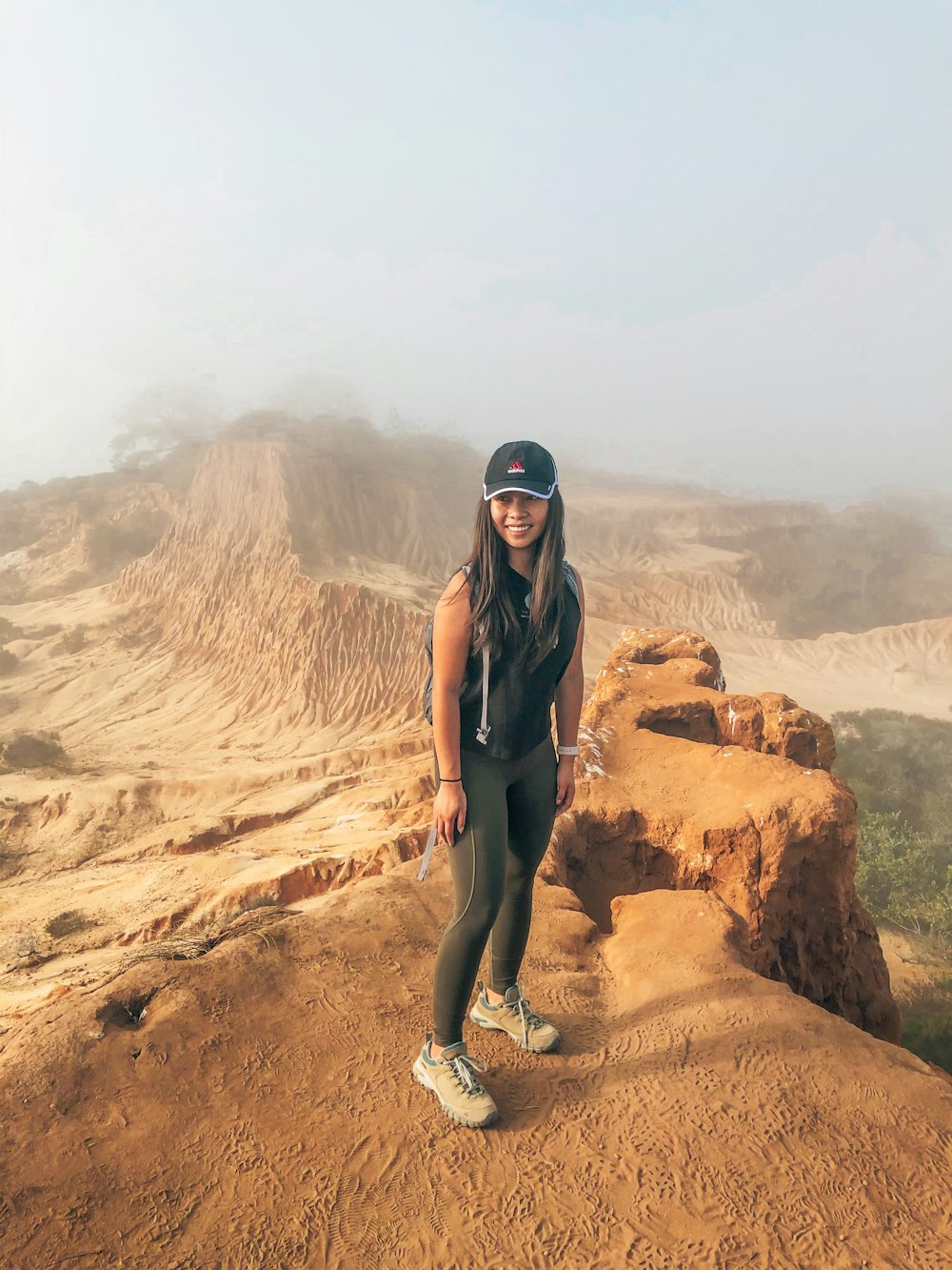 woman in black tank top and gray pants standing on brown rock formation during daytime