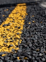 A close-up view of a rough asphalt surface with a textured yellow line running through it.