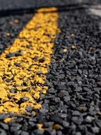 A close-up view of a rough asphalt surface with a textured yellow line running through it.