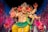 A colorful statue of a multi-armed deity adorned with jewelry and elaborate clothing, set against a vibrant, starry background. The deity has the face of an elephant and a small symbol on its palm, with various accessories enhancing its divine appearance.