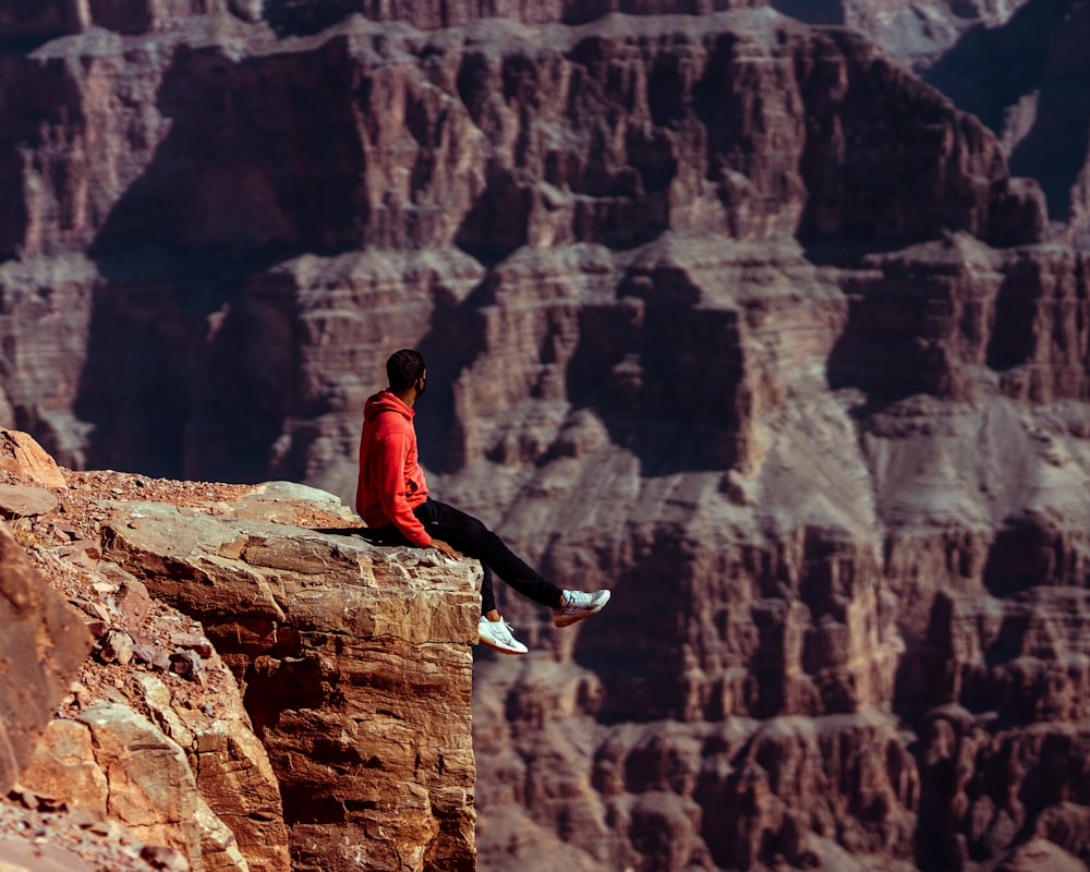 man in black jacket sitting on brown rock during daytime