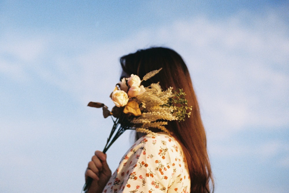 woman in white and blue floral long sleeve shirt holding bouquet of flowers