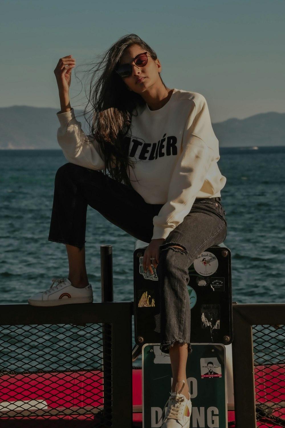 woman in white and black long sleeve shirt and black pants sitting on black metal fence