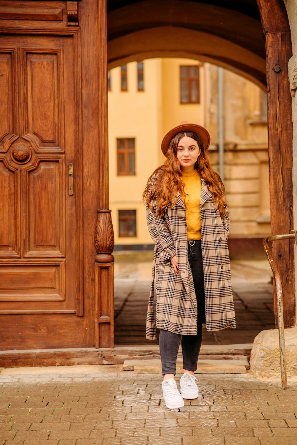 woman in black and white checkered coat standing beside brown wooden door during daytime