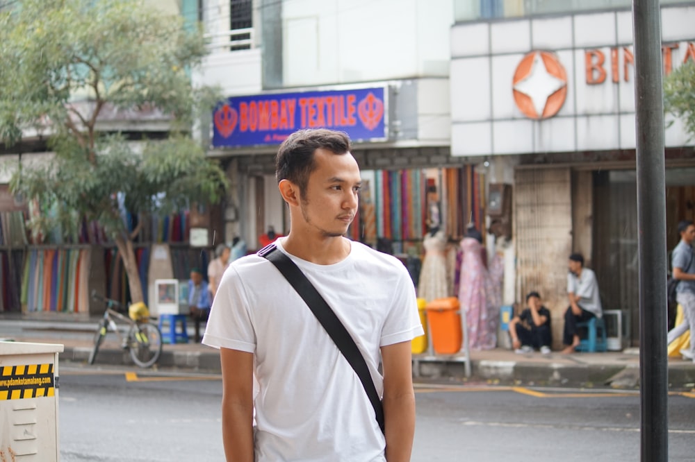 Mann in weißem Rundhals-T-Shirt, der tagsüber auf der Straße steht