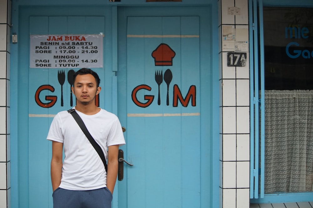 man in white crew neck t-shirt standing beside blue wall