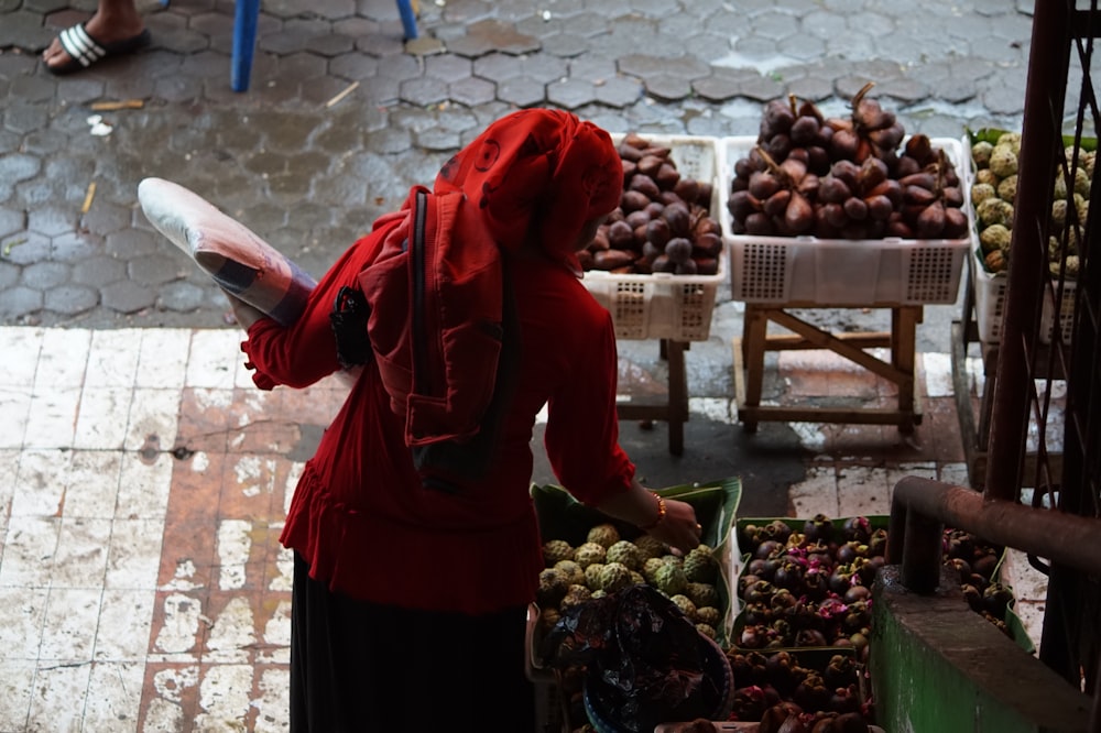 woman in red hoodie standing in front of fruit stand