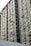 A high-rise residential building features numerous windows and balconies, with multiple clothes drying on rods extending from the windows. The facade consists of muted green panels with white framing creating a grid-like pattern.