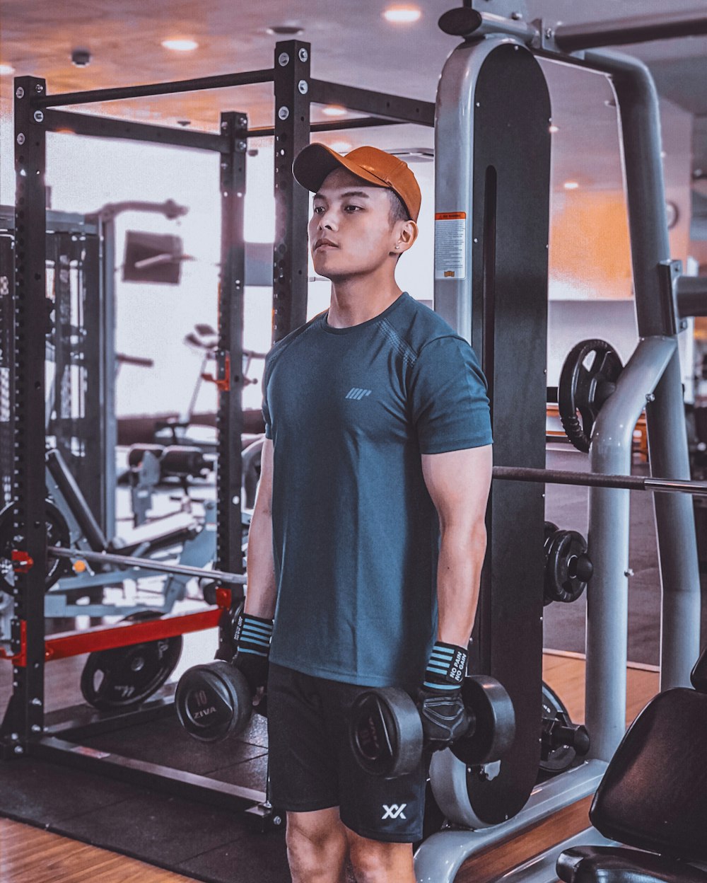 homme en t-shirt à col rond bleu et pantalon noir portant des haltères noirs et gris