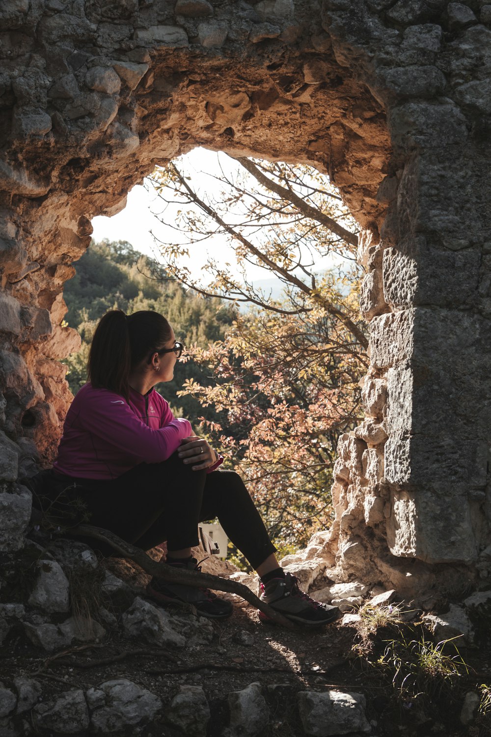 mulher na camisa roxa da manga comprida sentada na rocha durante o dia