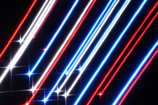 Bright diagonal lines in red, white, and blue intersect against a dark background, creating a vibrant light pattern. Each line sparkles at regular intervals, enhancing the dynamic and energetic appearance.