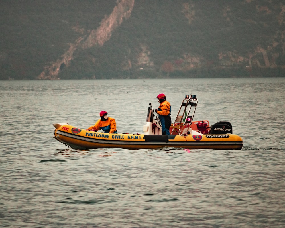 3 men riding on yellow and red kayak on body of water during daytime