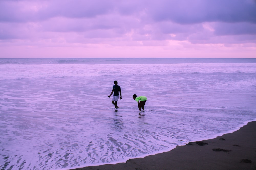 man and woman holding hands while walking on beach during daytime