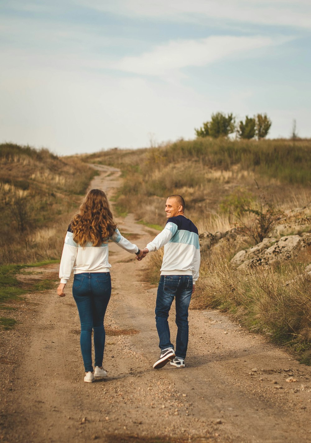 man and woman holding hands while walking on dirt road