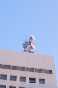 A building structure with a communication tower on top, featuring several satellite dishes against a clear blue sky.