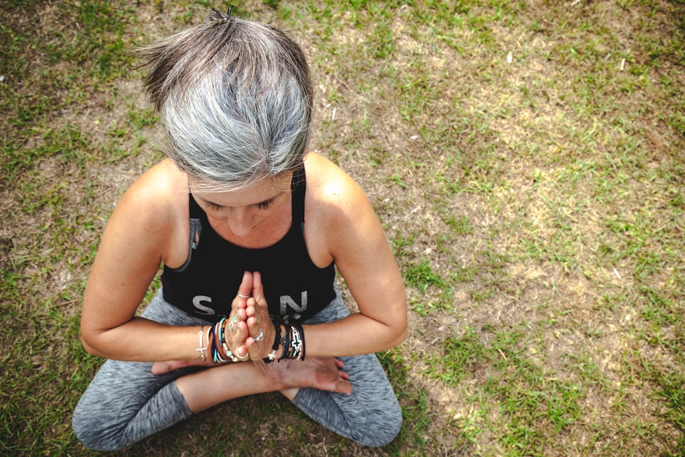 woman in black tank top and gray denim jeans sitting on green grass field during daytime