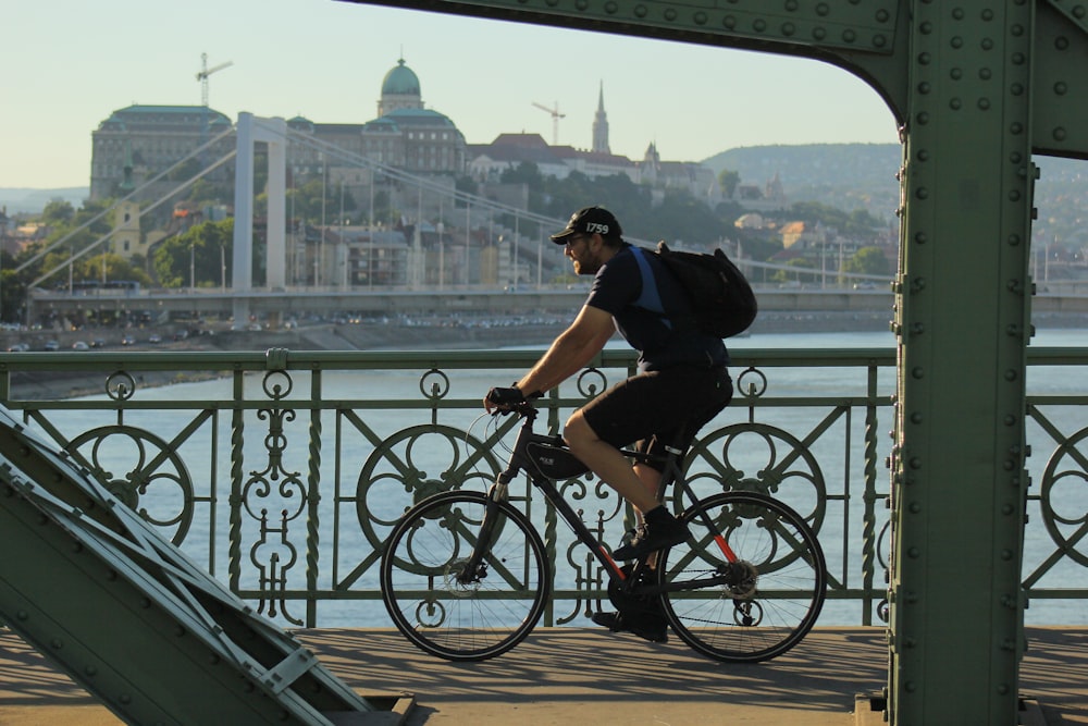 man in black t-shirt riding on bicycle near body of water during daytime