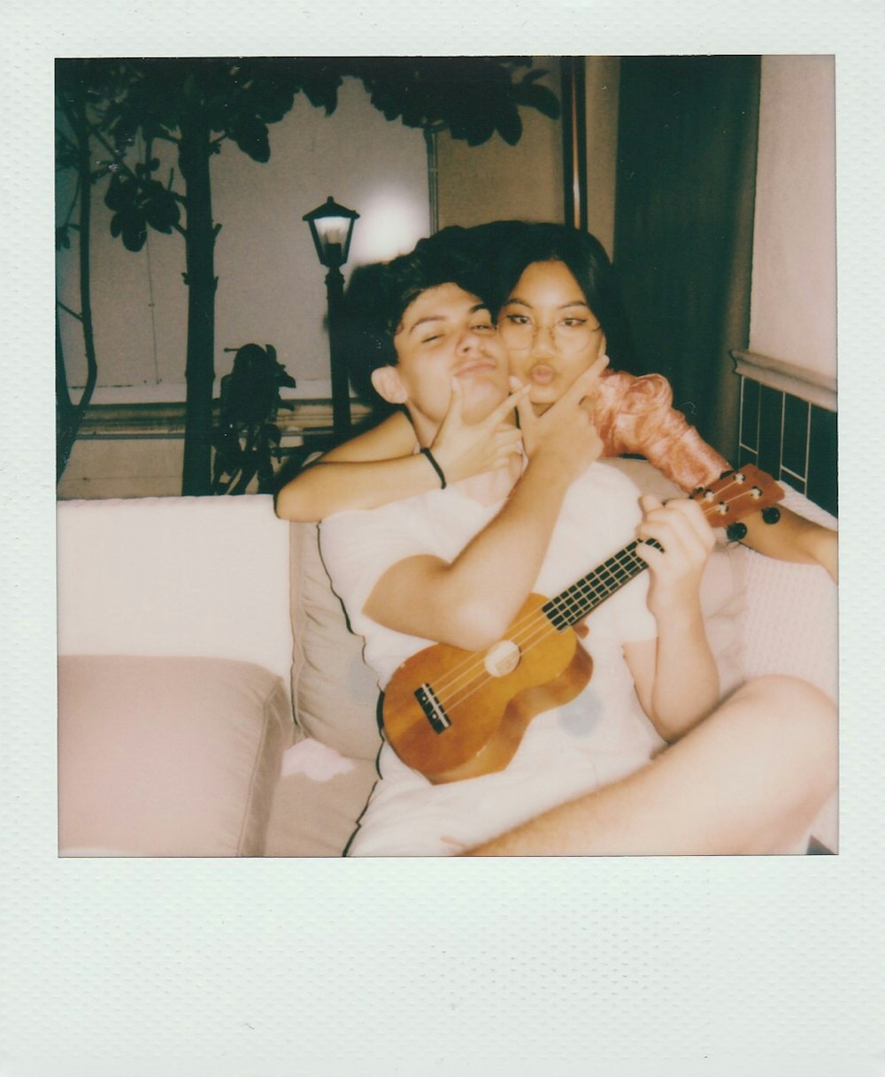 woman in white tank top sitting on white sofa chair holding brown acoustic guitar