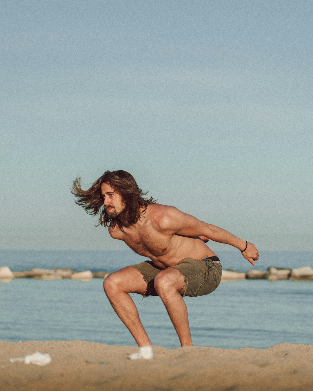 topless woman sitting on brown rock near body of water during daytime