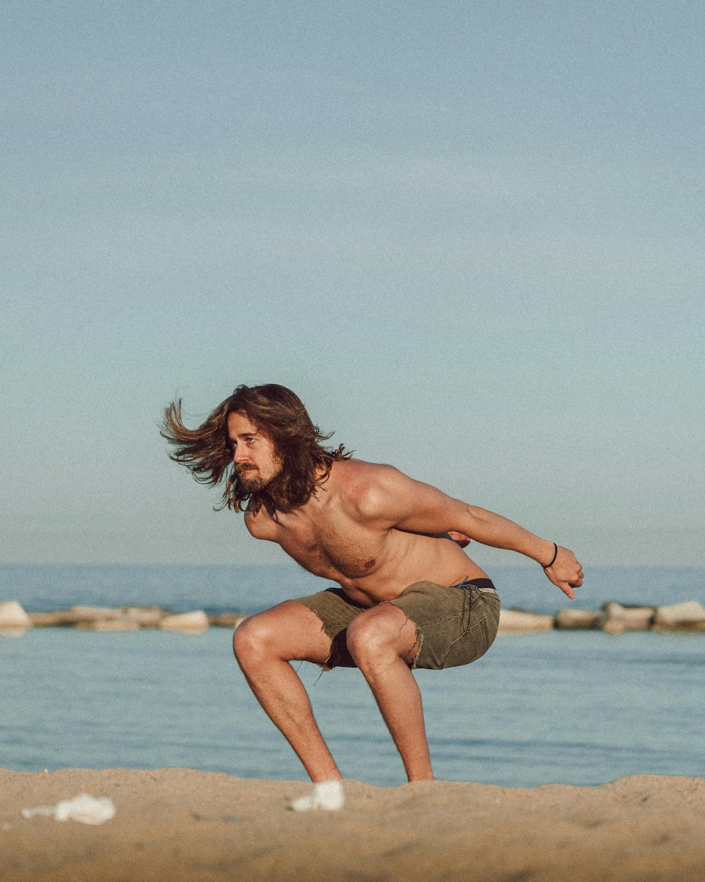 topless woman sitting on brown rock near body of water during daytime