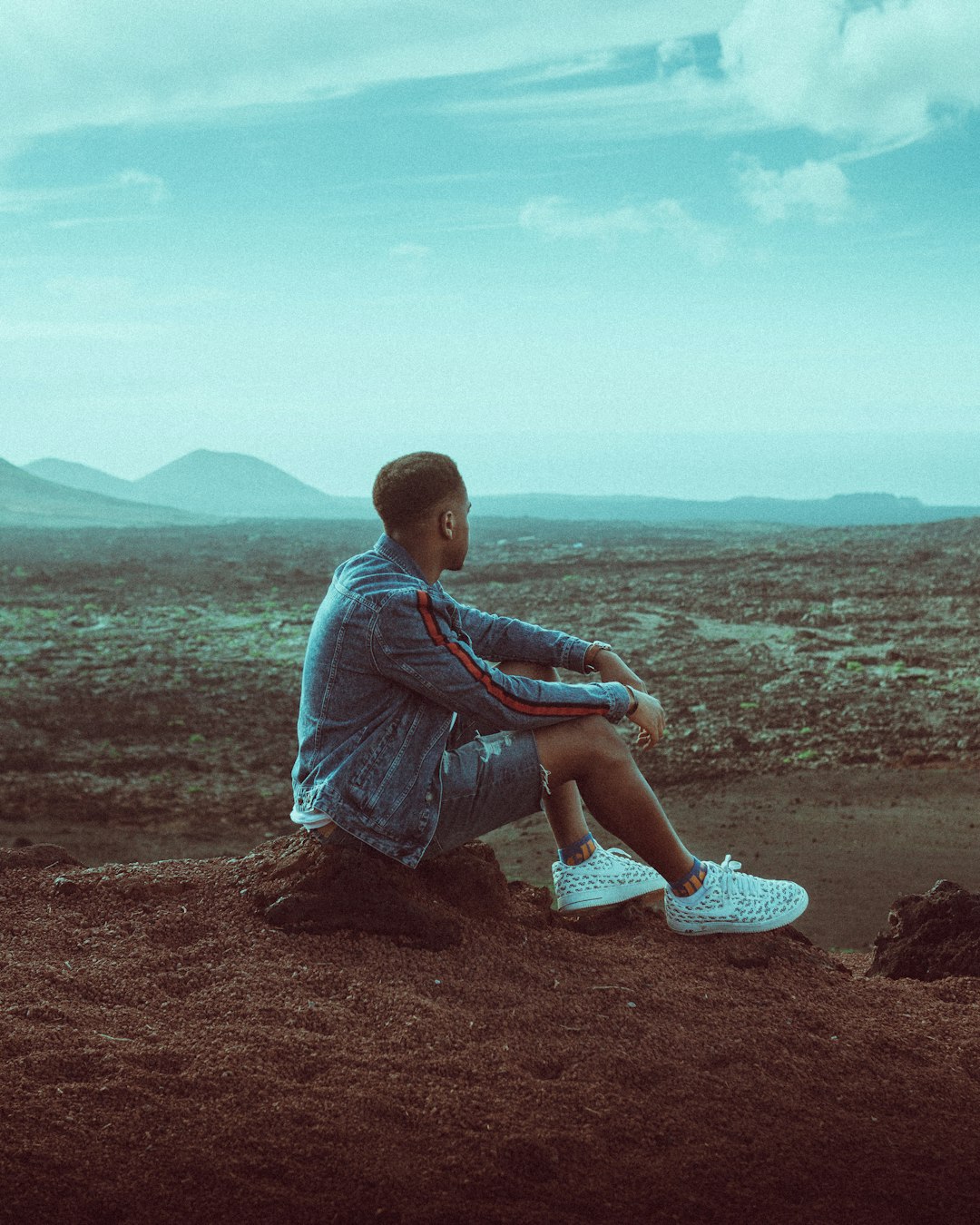 man in blue t-shirt sitting on brown sand during daytime