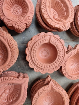 A collection of intricately designed terracotta oil lamps, also known as diyas, arranged closely together. Each lamp features detailed patterns and carvings, showcasing traditional craftsmanship.