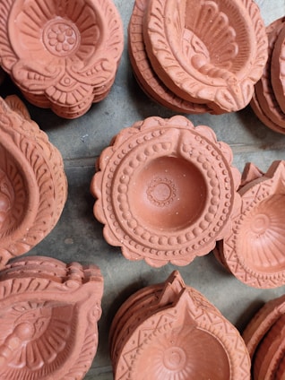 A collection of intricately designed terracotta oil lamps, also known as diyas, arranged closely together. Each lamp features detailed patterns and carvings, showcasing traditional craftsmanship.